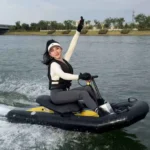 Woman riding black yellow inflatable motorized jet kayak on river, portable electric water sports vessel