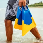 Lifestyle beach shot adult holding blue orange dolphin silicone swim fins shallow ocean water snorkeling training gear real use photo