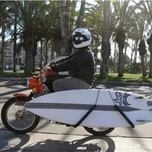 Retro motorbike with installed surfboard rack carrying white surfboard on palm-lined beach street, real-world surf carrier usage demo